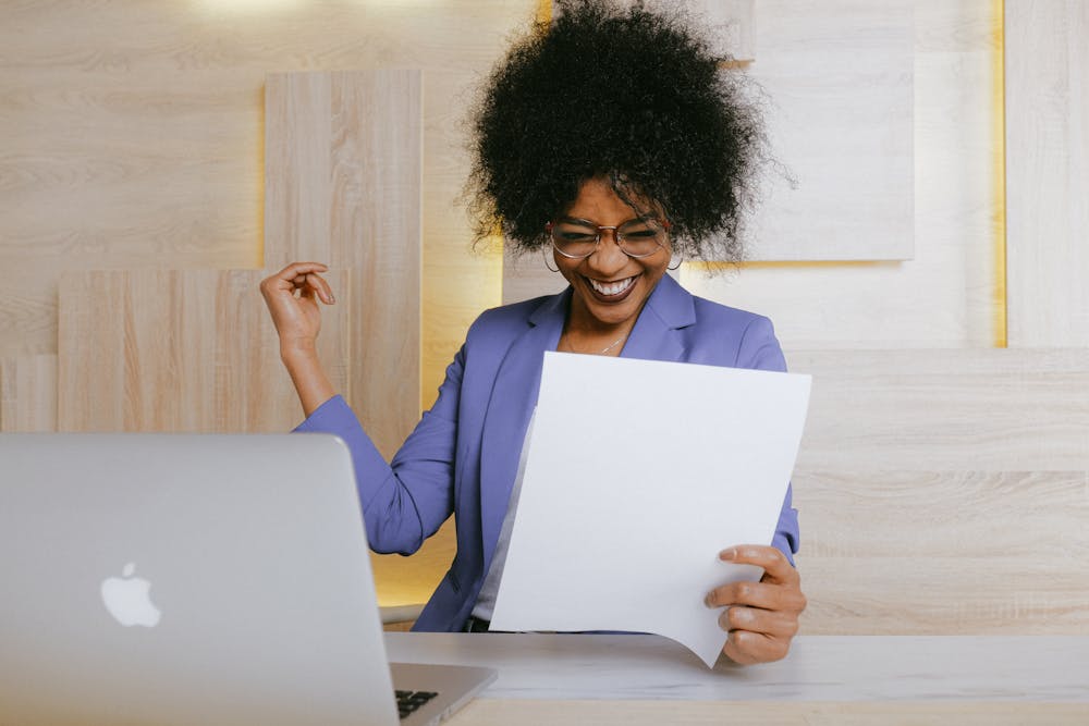 woman in lavender jacket looks at a paper and celebrates