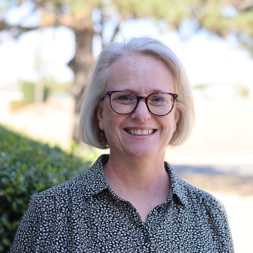 woman with light chin-length hair and glasses standing outside