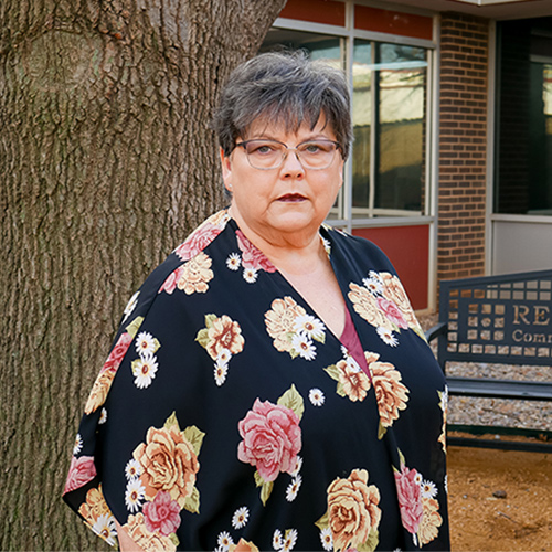 Woman in floral shirt standing in front of a tree