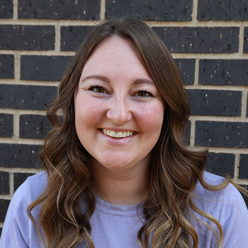 Woman with long brown hair wearing a purple shirt