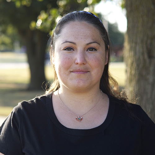 Woman with long dark hair pulled back with a headband wearing a heart necklace and black shirt