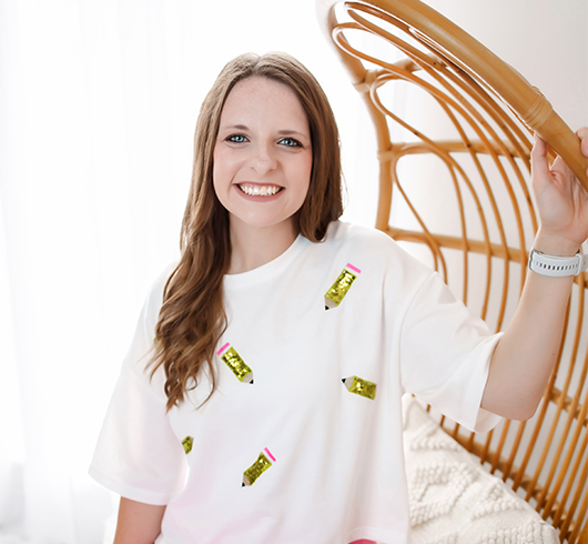Woman in a white shirt with cartoon pencils on it, sitting on a wicker chair