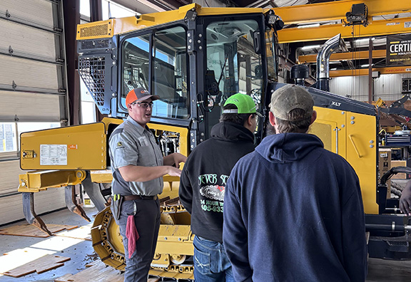Mechanic shows two individuals heavy machinery