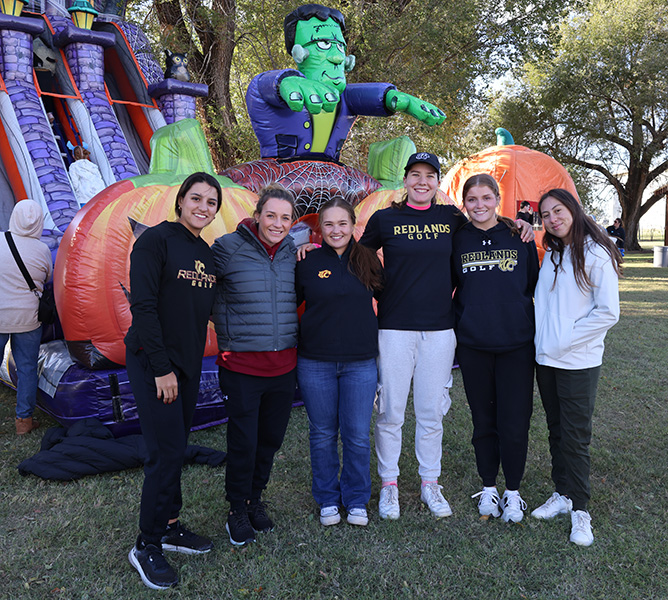 Women's golf team standing in front of a Frankenstein inflatable slide