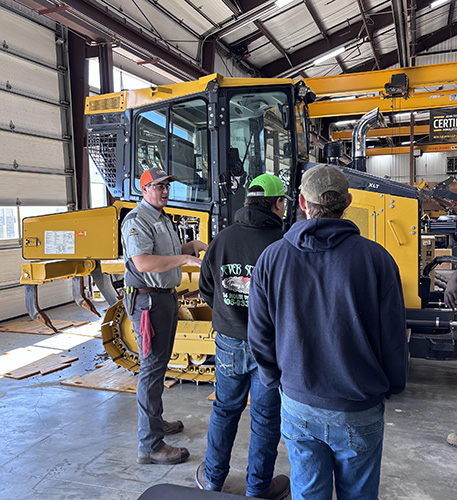 Three men in hats standing in front of heavy machinery in a workroom