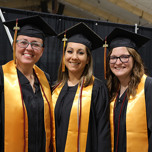 Three women with black graduation caps and gowns, and gold stohls