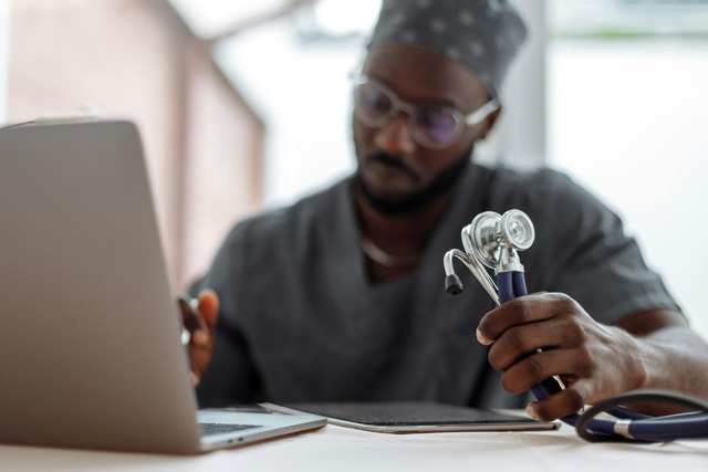 Black man in scrubs working on paperwork, holding a stethescope