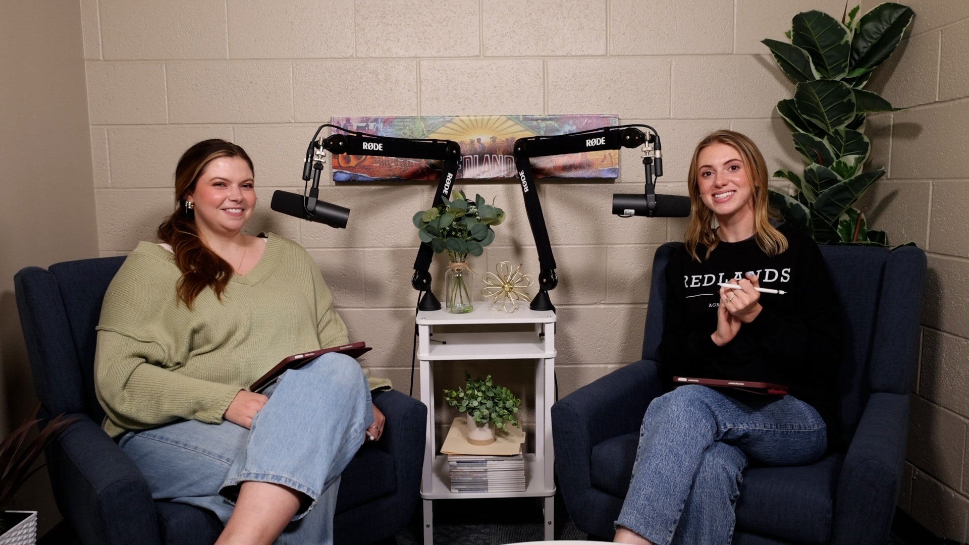 Two women smile and sit next to microphones