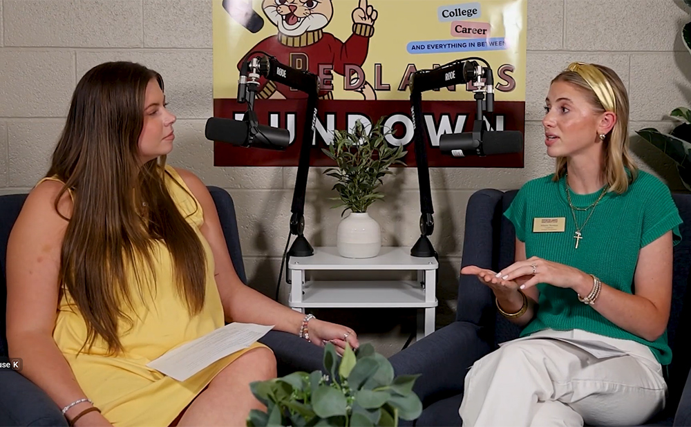 Woman in yellow dress and woman in green shirt with white pants sit and discuss