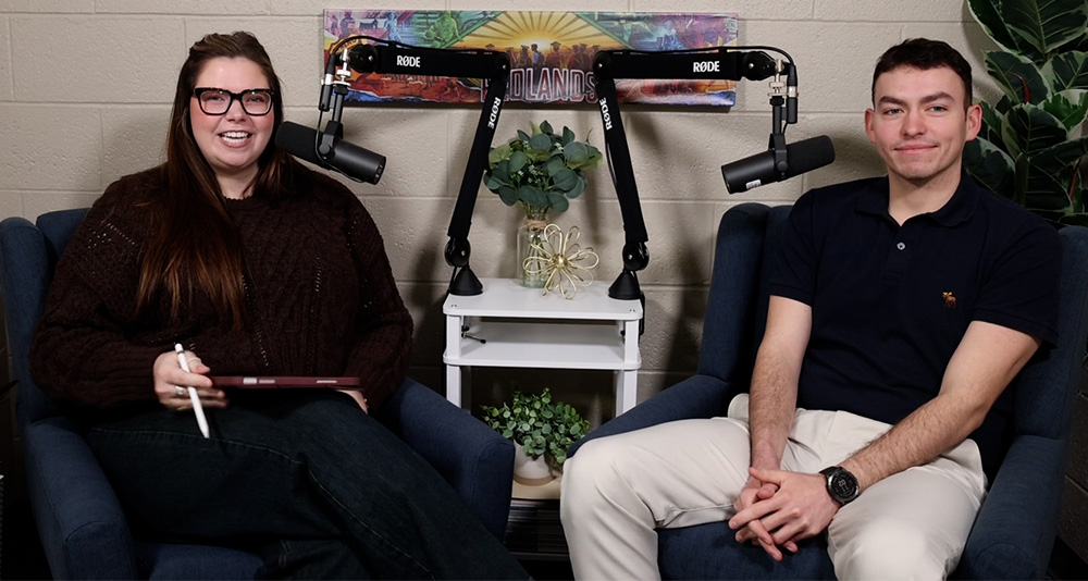Woman with black glasses sits next to a man with a dark navy polo shirt