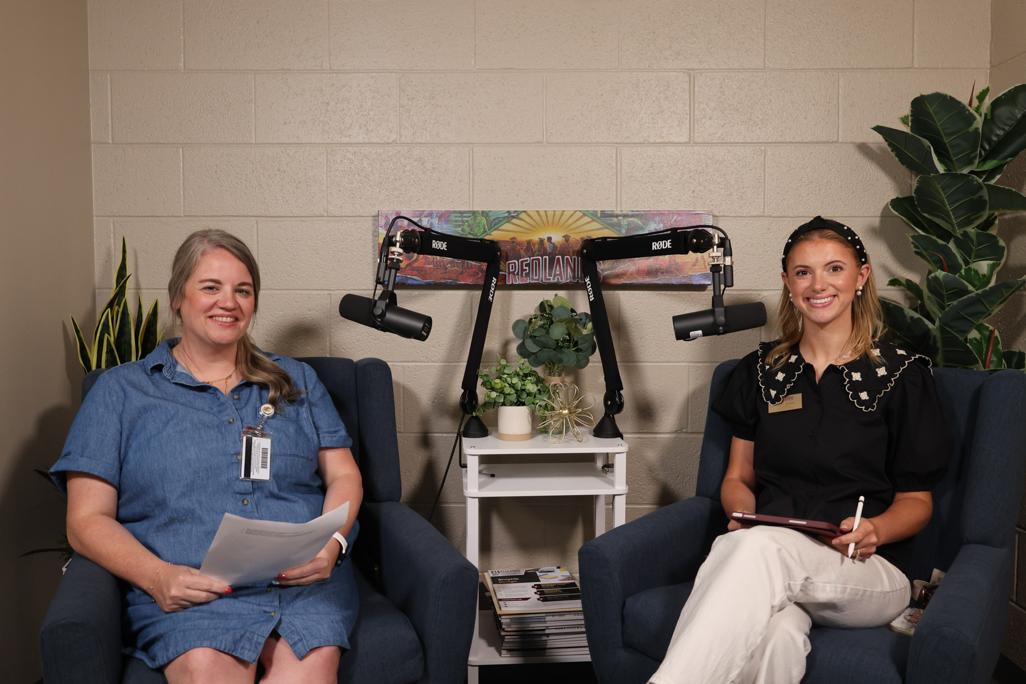 Two women smile and sit next to microphones