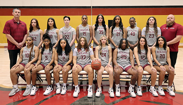 Redland's 2024 Women's Basketball team poses together in grey uniforms with red text and trim, with the coaches standing on each side of the group.
